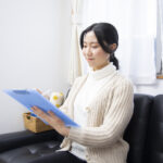 ソファに座った女性が、青いクリップボードの用紙にペンで記入している様子
